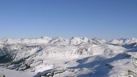 Luz-Del-Sol-A-Través-De-Crestas-De-Montañas-Nevadas-Contra-El-Cielo-Azul-Claro-En-Canadá