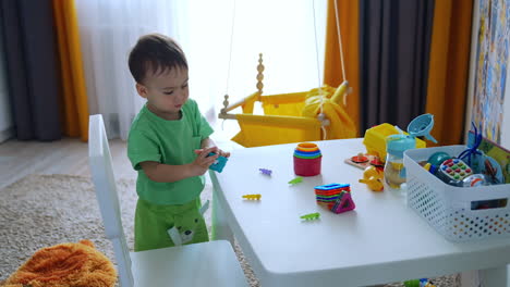 caucasian toddler standing in the room near the desk. beautiful kid plays with the bright toys.