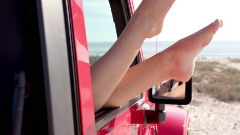 bare feet protrude from a red vehicle's window at the beach on a road trip