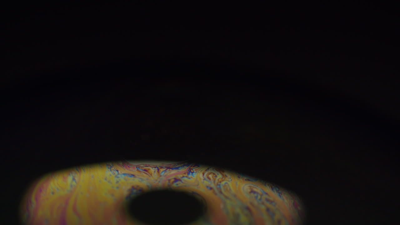 Light patterns emerging on a small soap bubble revealing abstract forms and shapes on the sphere