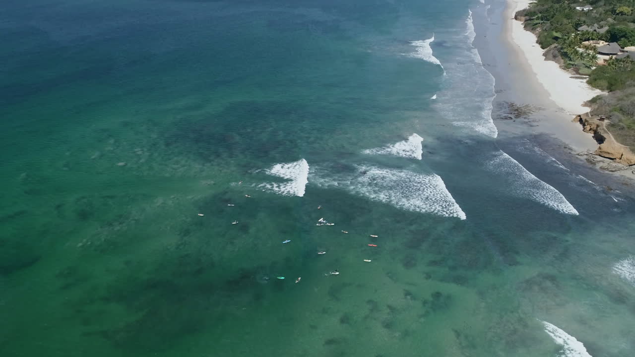 Luftopptak som panorerer opp fra en gruppe surfere og avslører en solrik kyst, 4K