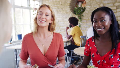 multi ethnic group of three  female friends laughing and talking over brunch in a busy restaurant, front view, close up