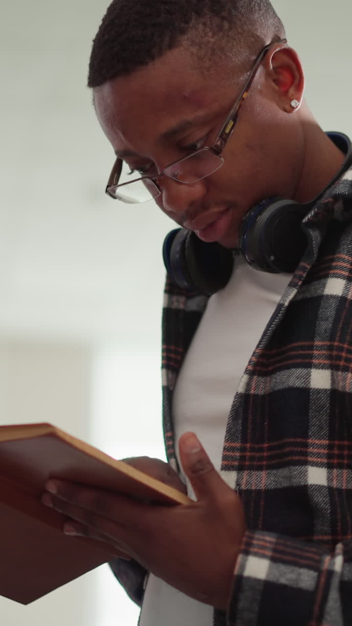 Hipster reads book in college library. African American man with textbook learns information by bookshelf. Passionate reader studies scientific literature