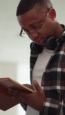 hipster reads book in college library. african american man with textbook learns information by bookshelf. passionate reader studies scientific literature