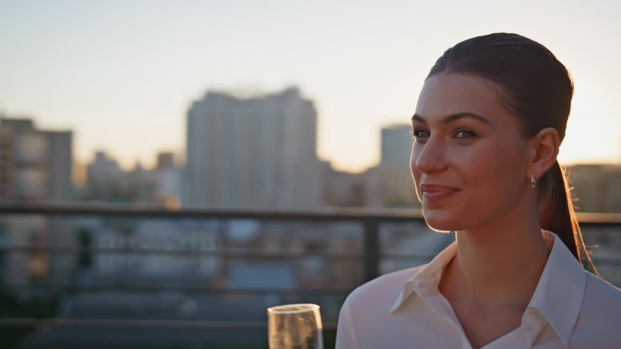 Elegant girl drinking champagne at sunset rooftop closeup. Smiling woman sipping