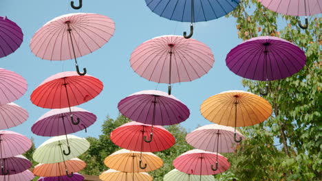 colorful umbrellas hanging against blue sky at summer sity festival - slow motion dolly in low angle view