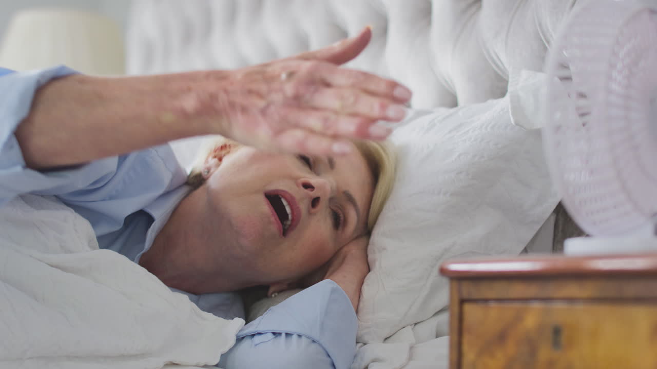 집에서 전기 팬을 사용하여 침대에서 불면증을 고 있는 폐경기 성숙한 여성