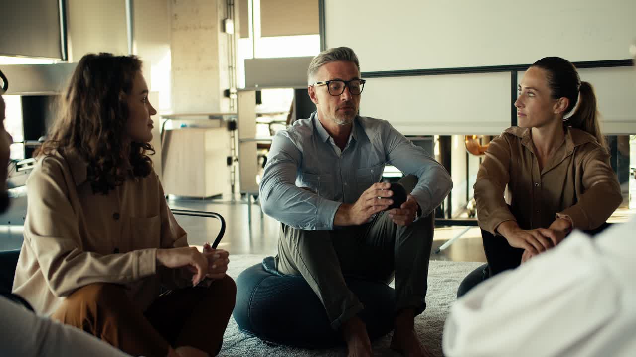 un hombre de mediana edad de cabello gris con gafas y un traje de negocios habla sobre su experiencia en la terapia de grupo en la oficina