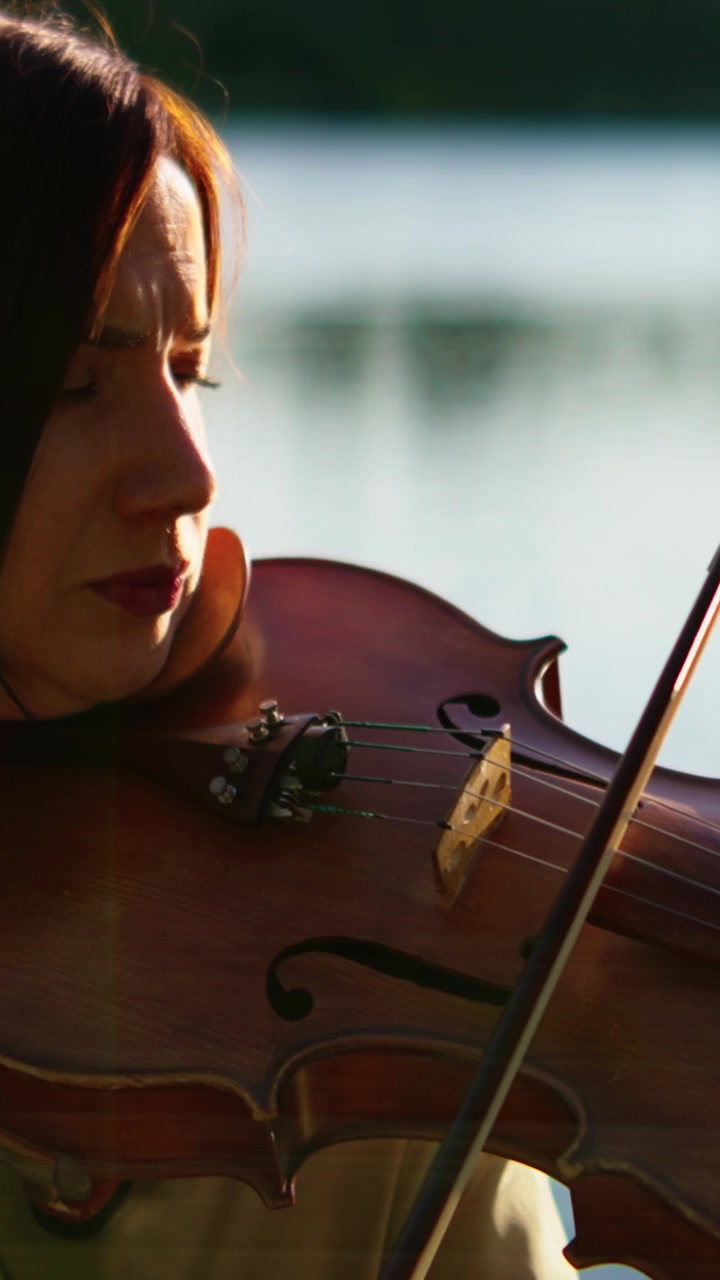 Woman Playing Violin Outdoors by a Lake