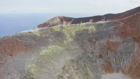 aerial view flying over volcano, tilt down camera toward colorful crater, close up zoom on sulfuric smokes. volcano island