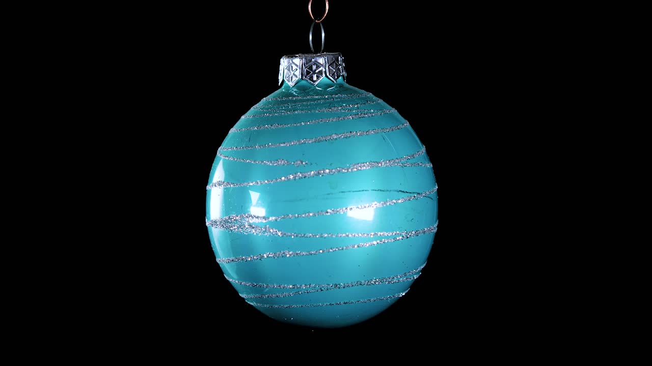 Einzelne blau-türkise Weihnachtskugel mit Glitzerstreifen und schwarzem Hintergrund, Nahaufnahme.