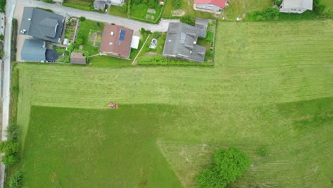 Tractor-mowing-green-grass-beside-family-hoses-settlement