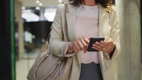 Caucasian-businesswoman-using-smartphone-in-corridor-of-modern-office