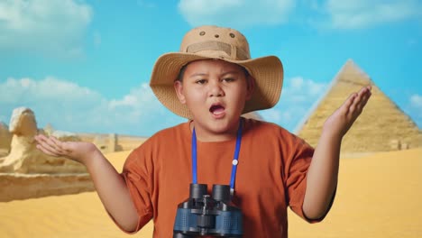 asian boy with a hat standing doubtfully and asking why after looking through the binoculars. boy researcher examines something while traveling in giza pyramid, travel adventure concept, close up