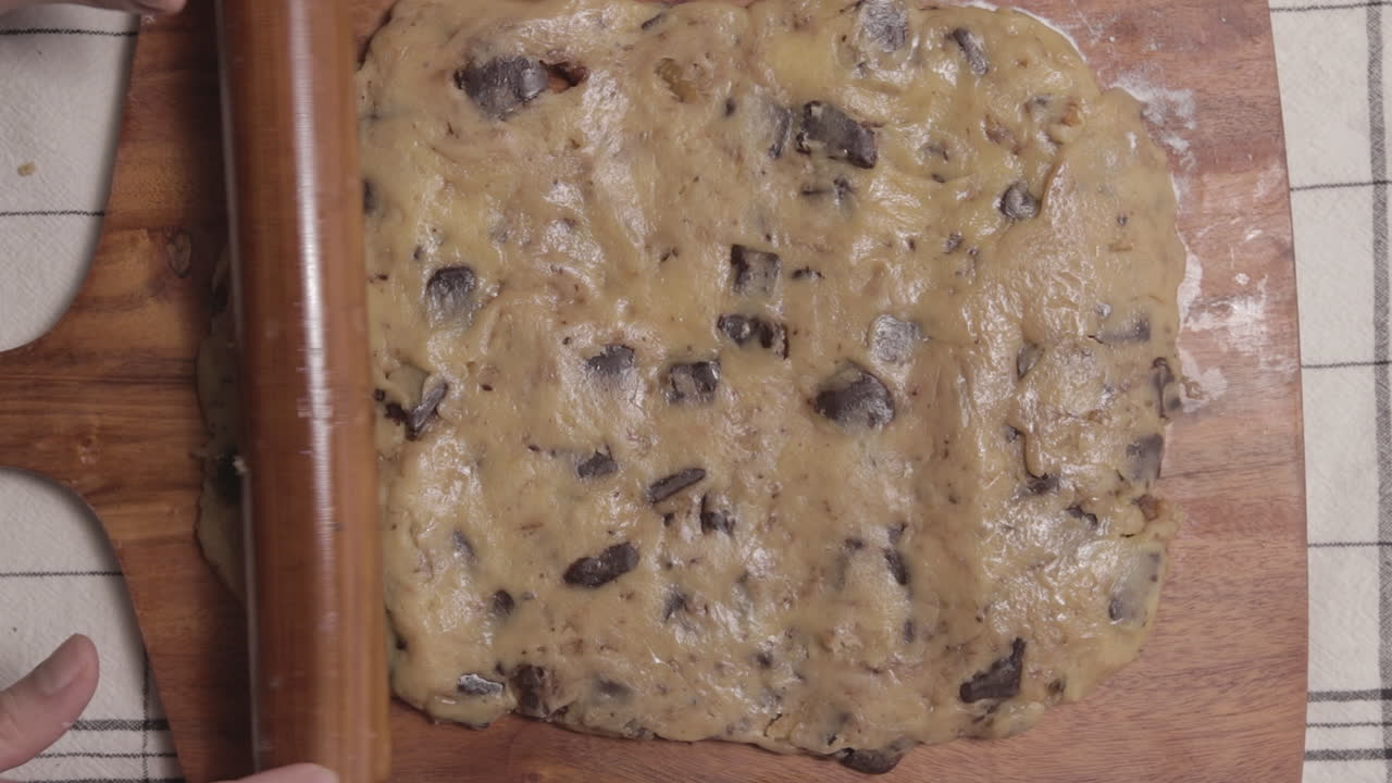 Rolling freshly made chocolate cookie dough on wooden board, top down view