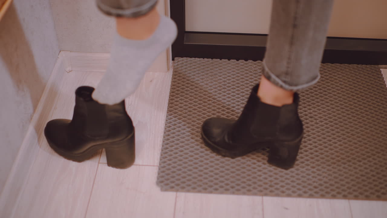 Close up of young woman in jeans finishing putting on black heeled shoes, adjusting last one by hand near mirror in hallway, preparing to leave home, showing everyday lifestyle