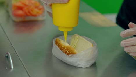 cu cocinero en cámara lenta prepara un perrito caliente vierte mayonesa en un rollo