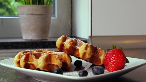disparo estático de deliciosos gofres belgas decorados con arándanos frutales y fresas mientras se agrega azúcar en polvo dulce en la cocina