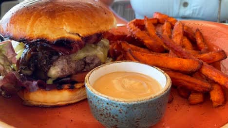 Deliciosa-Hamburguesa-Con-Queso-Con-Pan-Brioche-Y-Batatas-Fritas-Con-Salsa-De-Mayonesa-Picante,-Restaurante-De-Comida-Rápida,-Toma-De-4k