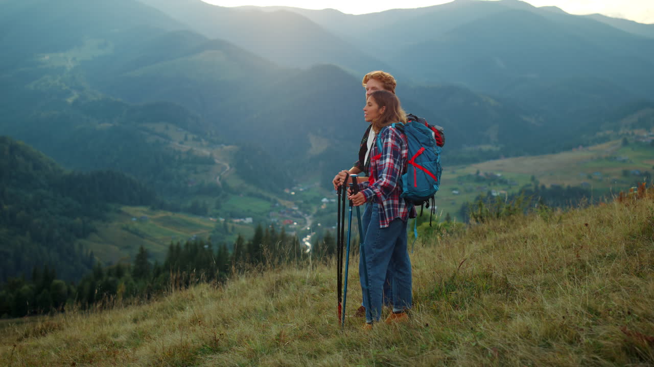 Couple backpackers enjoy landscape mountain view. Two hikers relax on green hill