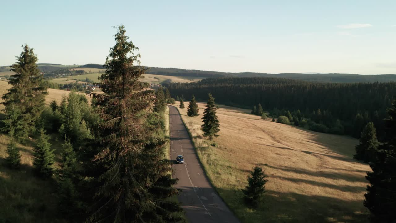 vista aérea de un solo coche conduciendo hacia la cámara en una carretera vacía en una agradable tarde de verano