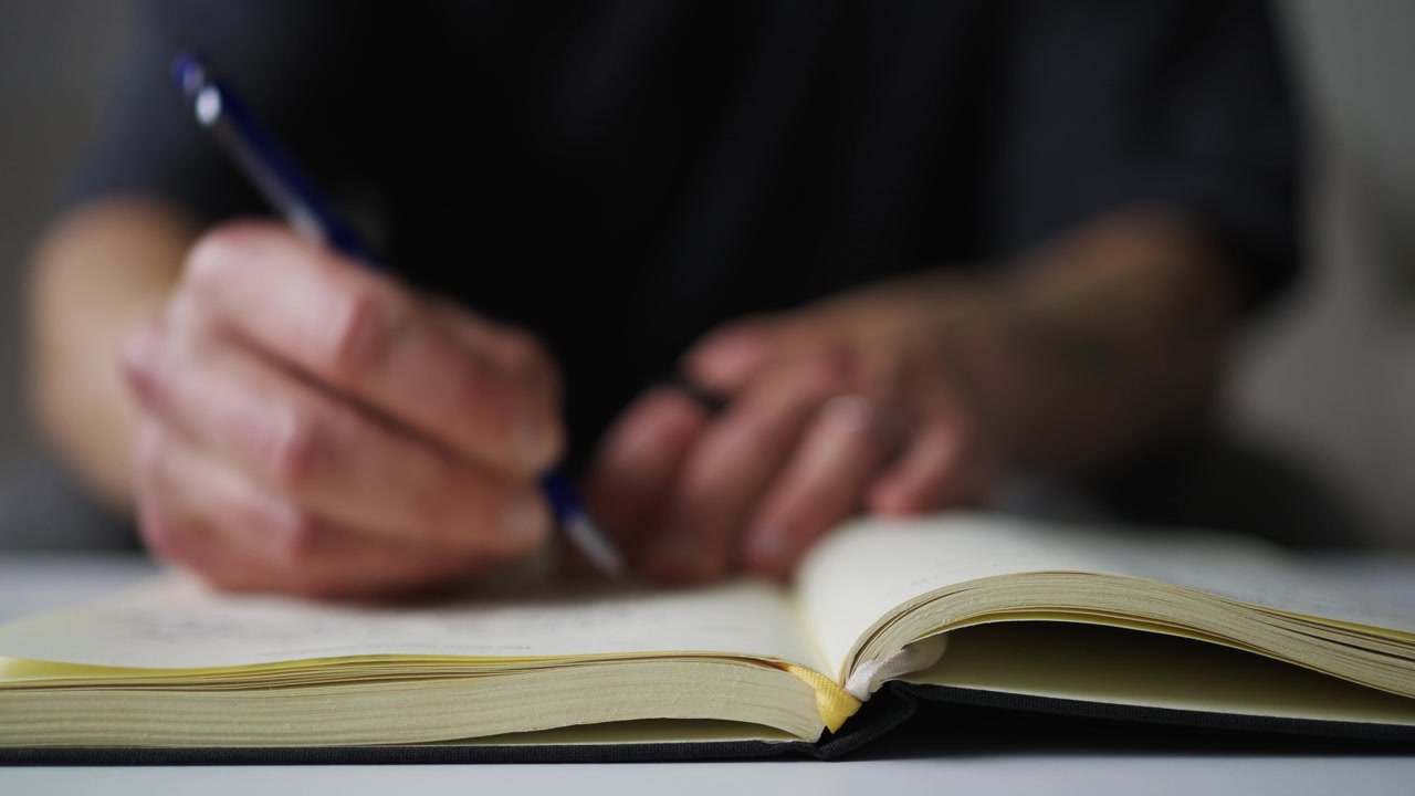 Close up of hands writing productivity journal on paper notebook.