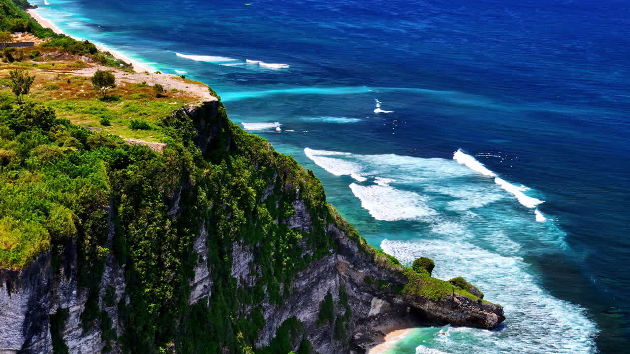 Rocky cliff with foamy ocean water and green foliage, aerial view