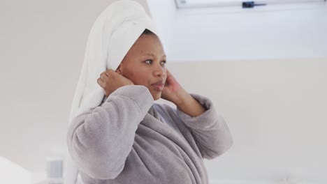 Happy-african-american-plus-size-woman-wearing-towel-on-head-in-bathroom,-unaltered,-slow-motion