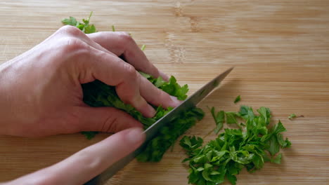 A-close-up-of-chopping-parsley-with-a-knife-on-a-wooden-board