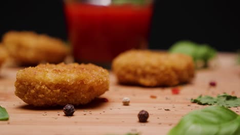 close up of chicken nuggets and sauce on a wooden cutting board, vegan, with green leaf and peppercorn garnish, black background, backing up dolly shot