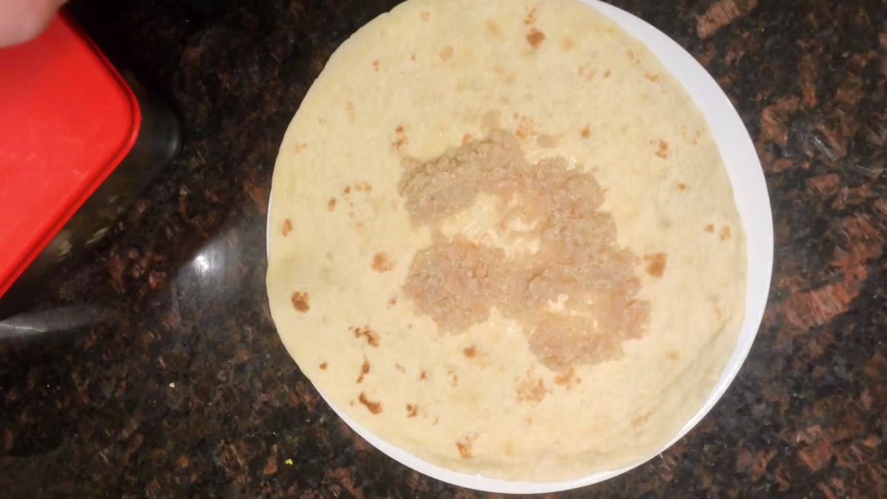 Close up top view footage captures a man preparing a rice and red beans tortilla wrap in a home kitchen