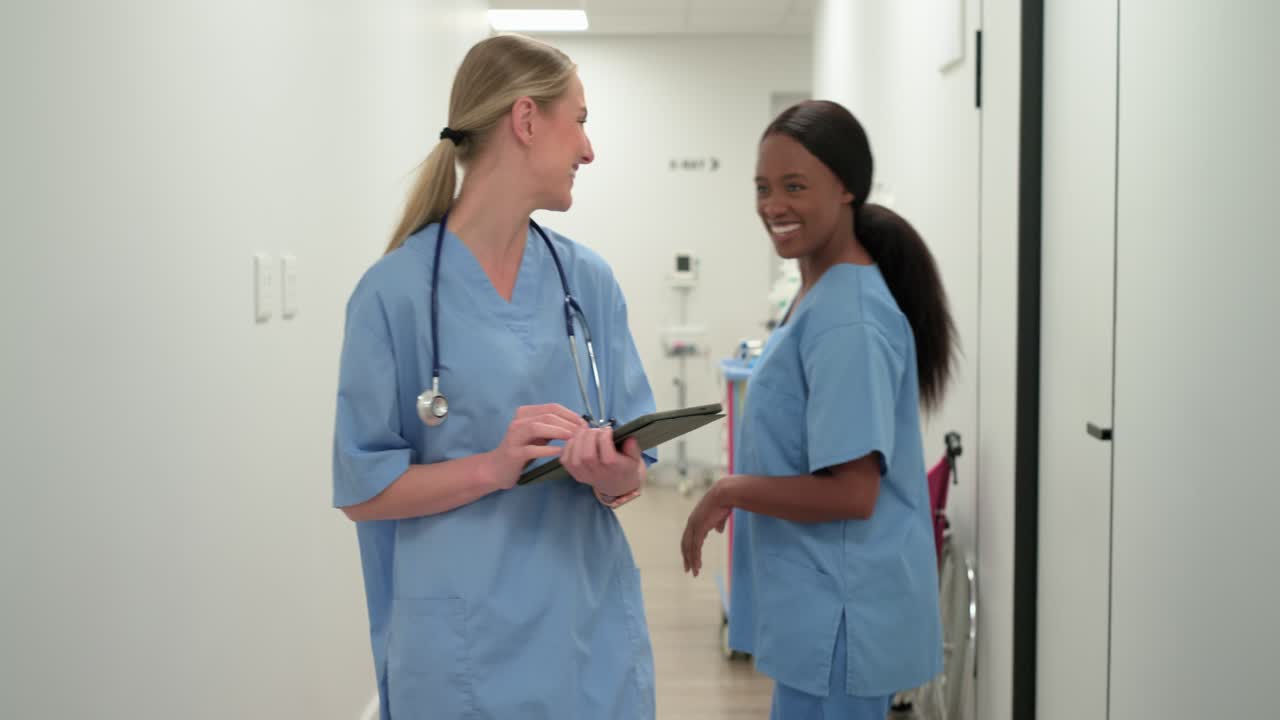 Diverse female nurses in scrubs walking hallway after MRI, lead RN tapping tablet reviewing scans