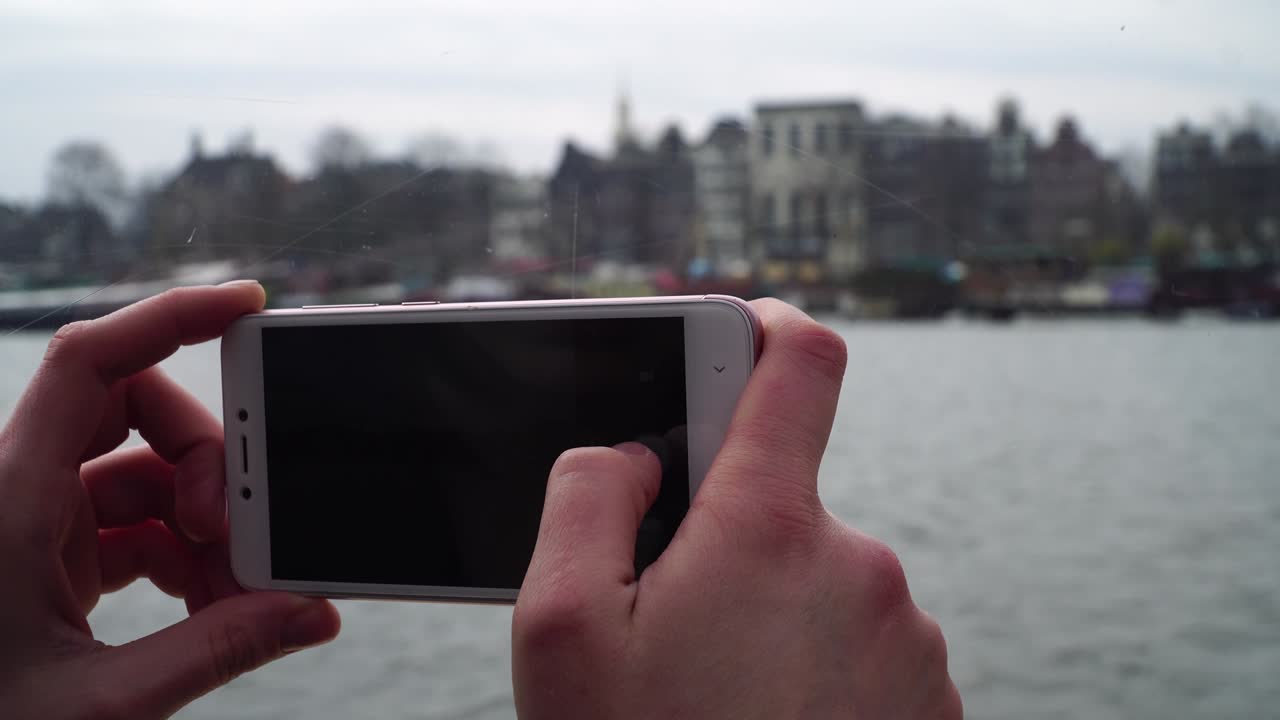chica navega en un barco a través de los canales de ámsterdam y toma fotos en el teléfono