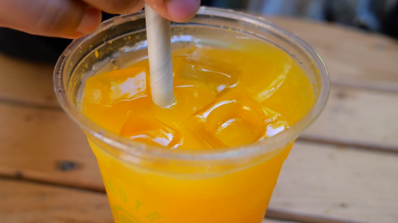 Close-up of a hand with a straw in a cup of iced orange juice