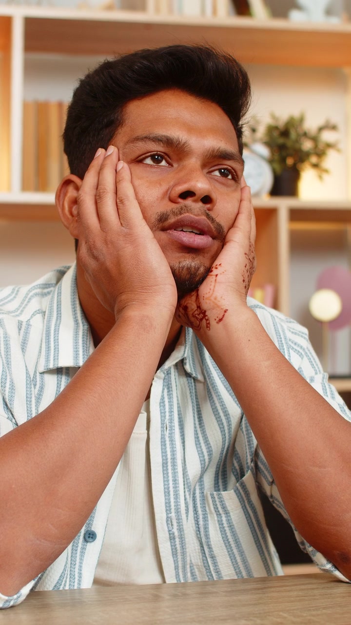 Indian man on home table leaning on hands looking exhausted after long remote work indoors at home