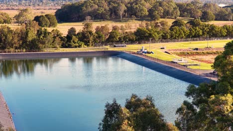 aerial camera smoothly pans across a large wastewater treatment pond surrounded by greenery at sunset, highlighting reflective water and industrial infrastructure