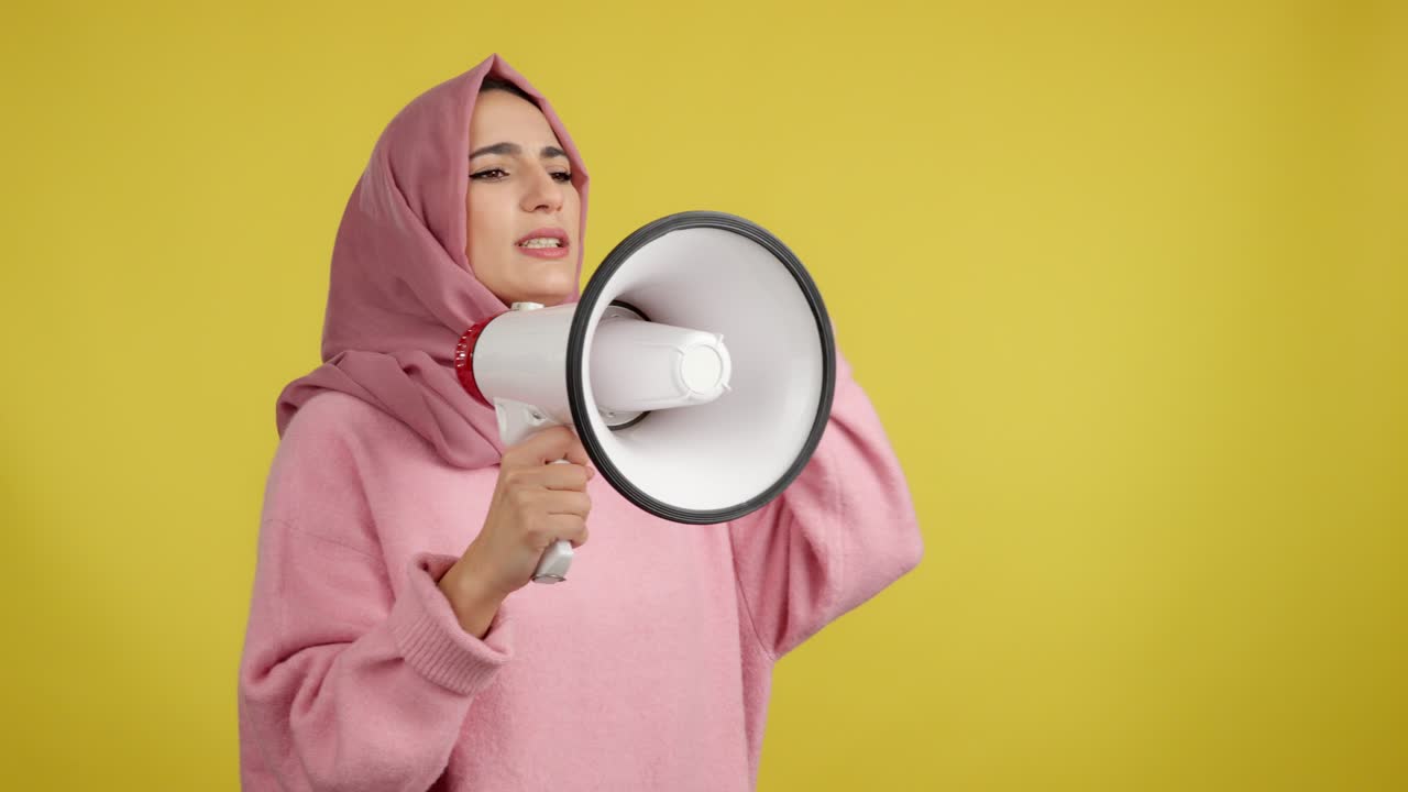 Woman in Hijab Speaking into a Megaphone on Yellow Background