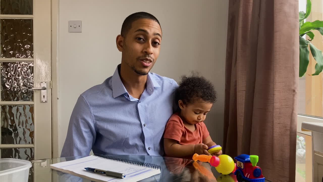 Giovane uomo con un bambino piccolo in videochiamata di lavoro che informa gli altri guardando direttamente in camera