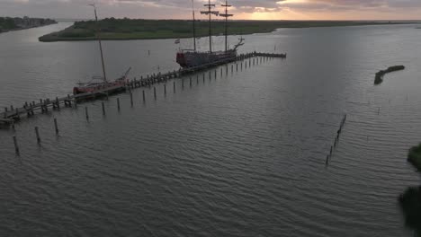 Reveal-shot-of-sail-boat-Soeverein-docked-in-the-harbour-of-Makkum-during-sunset,-aerial