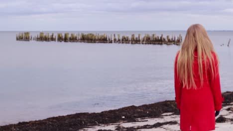 Side-view-of-old-wood-jetty-at-sea,-blond-hair-woman-walks-enters-shot