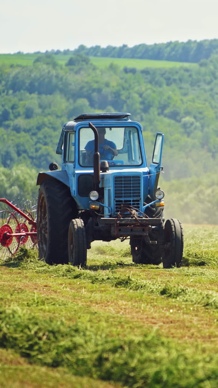 Front view of a tractor working on the field in summer. Agricultural machine changing dried grass on the natural field background. Vertical video