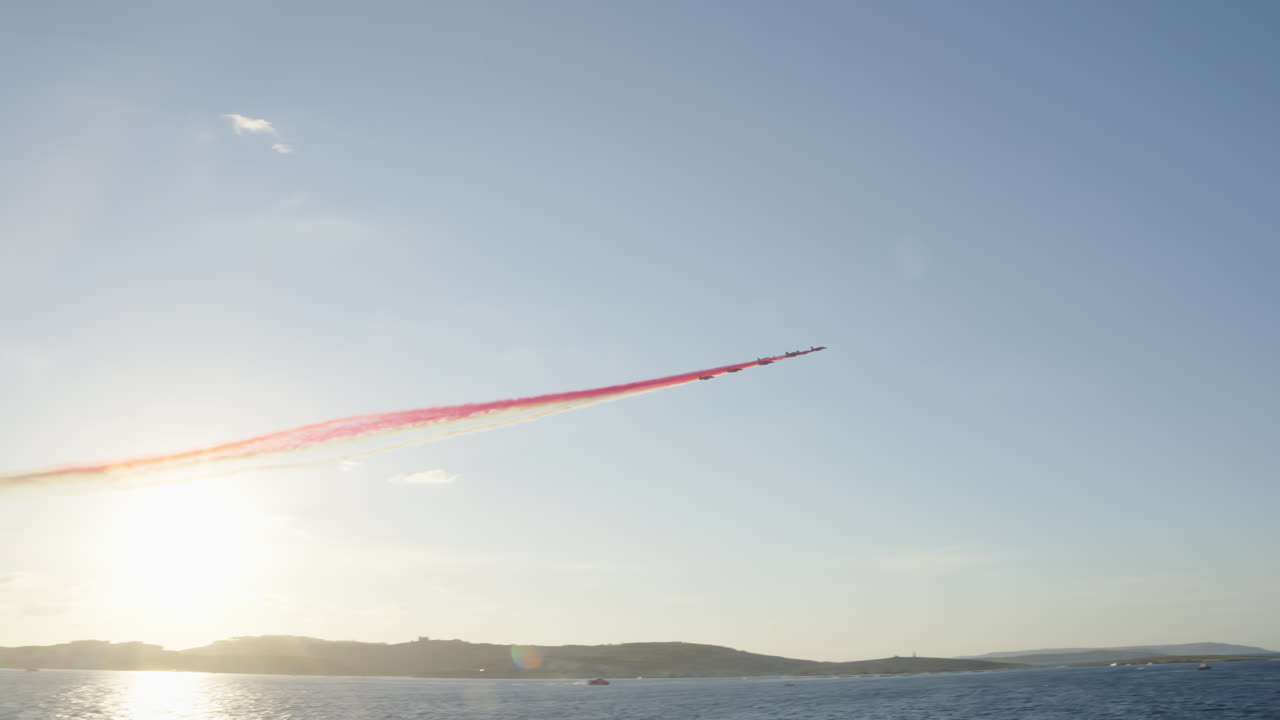 Jet che volano in formazione con scie di fumo rosse e bianche sull'oceano al tramonto