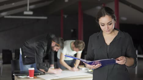 Portrait-of-a-fashionable-young-professional-woman-holding-folders-with-papers-in-a-stylish-contemporary-office.-Office-workers-on-the-background.-Shot-in-4k