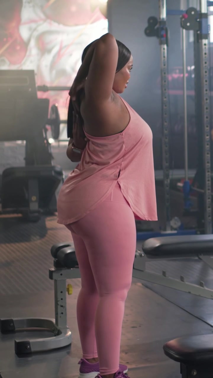 Vertical video: Rotating torso, adult woman warming up near bench in gym preparing ponytail in pink