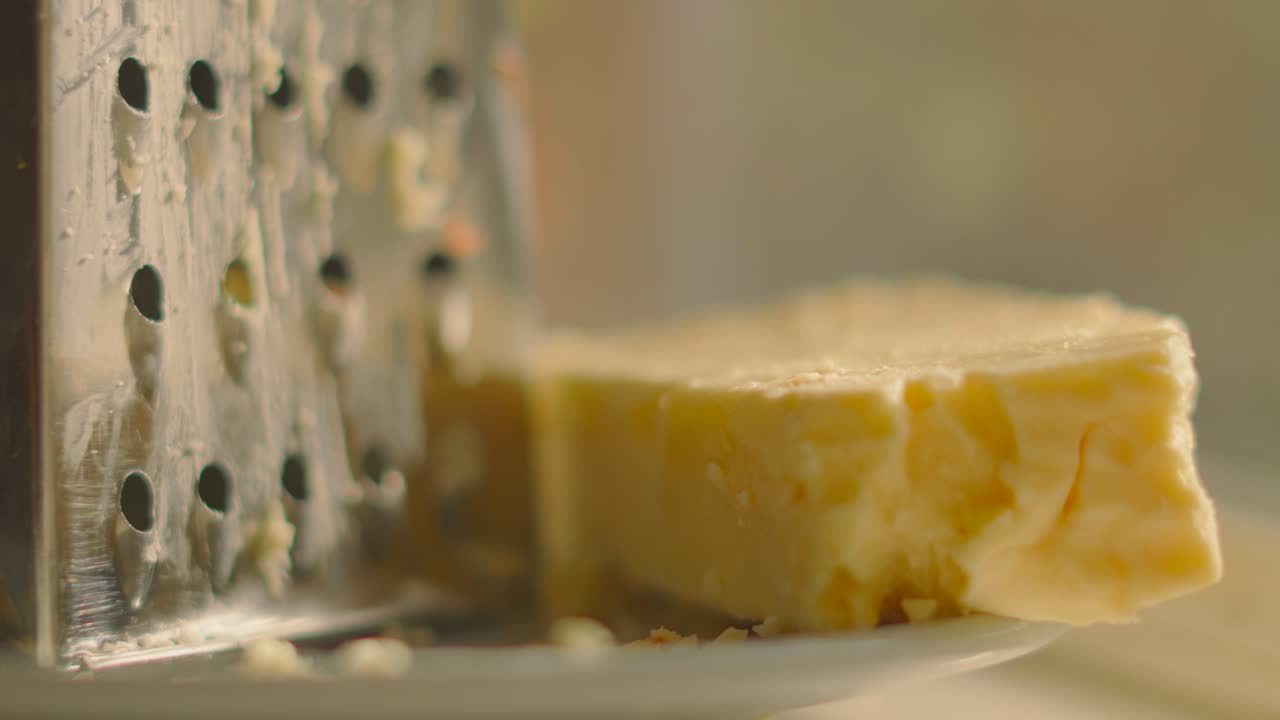 Slow Rotating Focus Pull Across Freshly Grated British Mature Cheddar Cheese Resting on Side Next to Grater in Soft Evening Light. Rustic Classic Food Setting with Cooking Ingredients