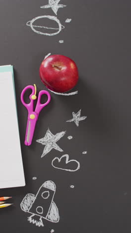 video vertical de la manzana y la papelería escolar con dibujos de tiza en fondo negro