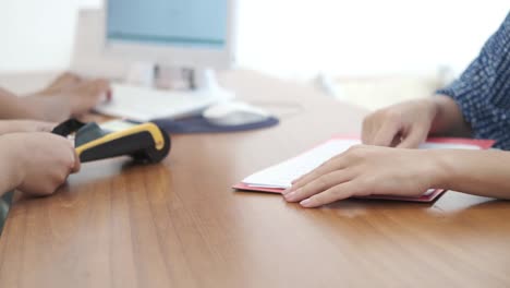 closeup of woman hands filling and signing document, agreement or contract on the desk and then giving credit card to sales person for payment. purchase of car, apartment, health insurance