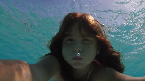 Selfie-Bajo-El-Agua-De-Una-Hermosa-Y-Linda-Niña-Pelirroja-Conteniendo-El-Aliento-Mientras-Flota-En-Agua-De-Mar-Transparente