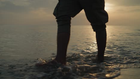 Mittlere-Aufnahme-Eines-Mannes,-Der-Bei-Sonnenaufgang-Am-Strand-Im-Wasser-In-Richtung-Der-Zeitlupe-Der-Kamera-Läuft