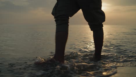 mid shot of male walking on the beach in the water at sunrise towards the camera slow motion